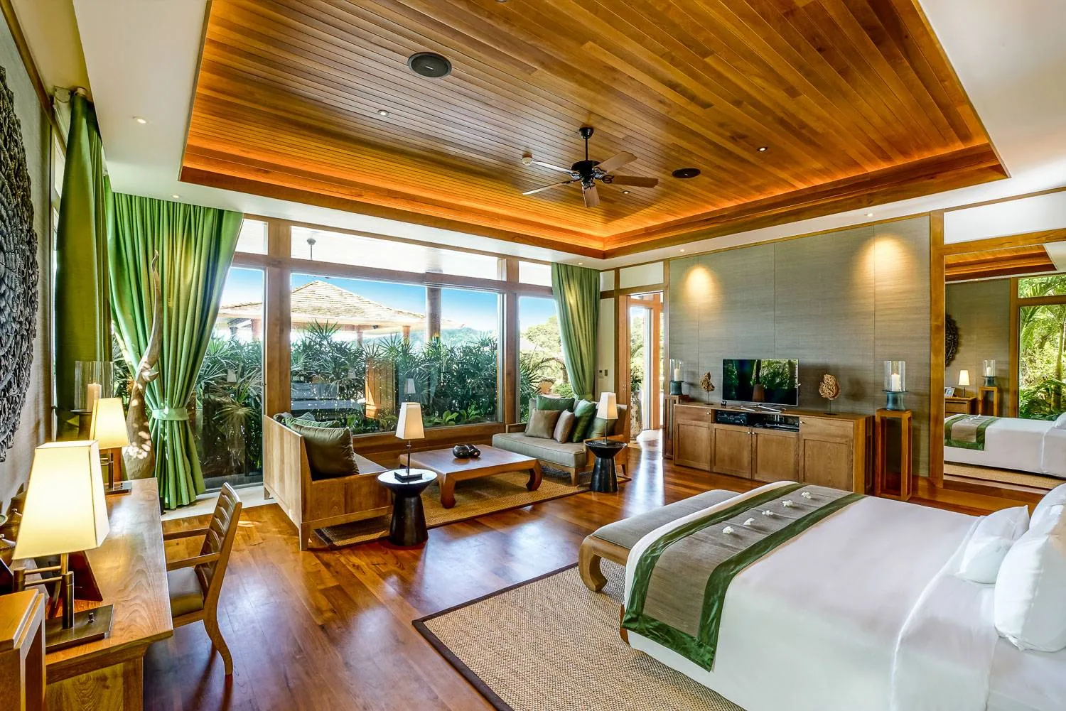 A bedroom with a bed, wood flooring, a sofa and a mirror, with an ensuite area visible