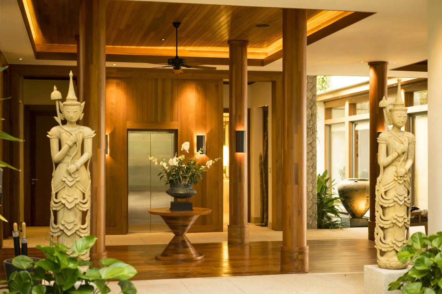 An entrance hall with carved wooden statues on either side and potted plants along the corridor
