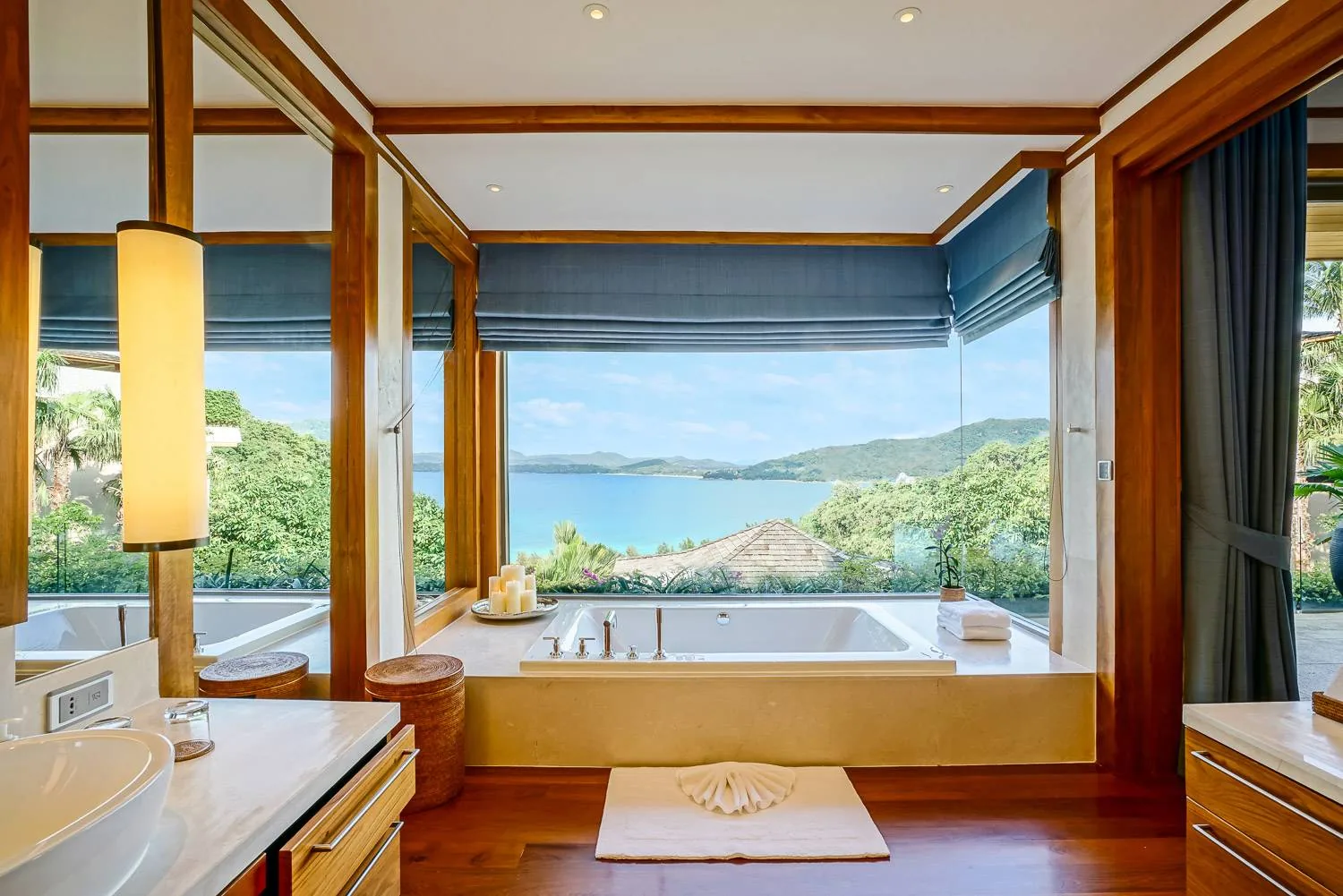 A bathroom with a freestanding tub positioned to face a window with a hillside and sea view