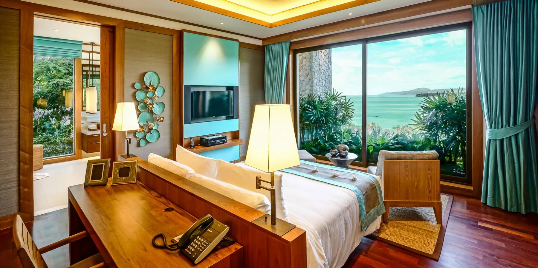 A bedroom with a work desk and telephone beside the bed, with a sea view through the window
