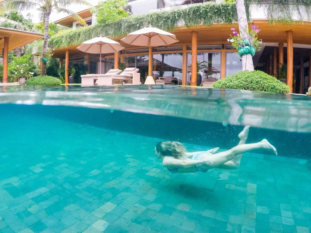 A half underwater photo of a woman swimming alone in a pool, with the villa building visible above the waterline