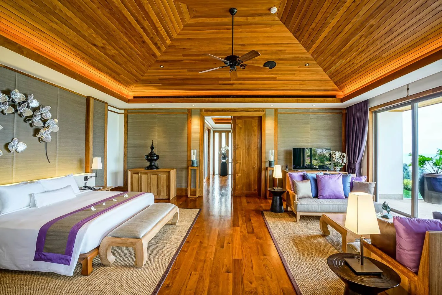 A bedroom with a bed, a sofa, a television unit and wood flooring, with sea facing windows