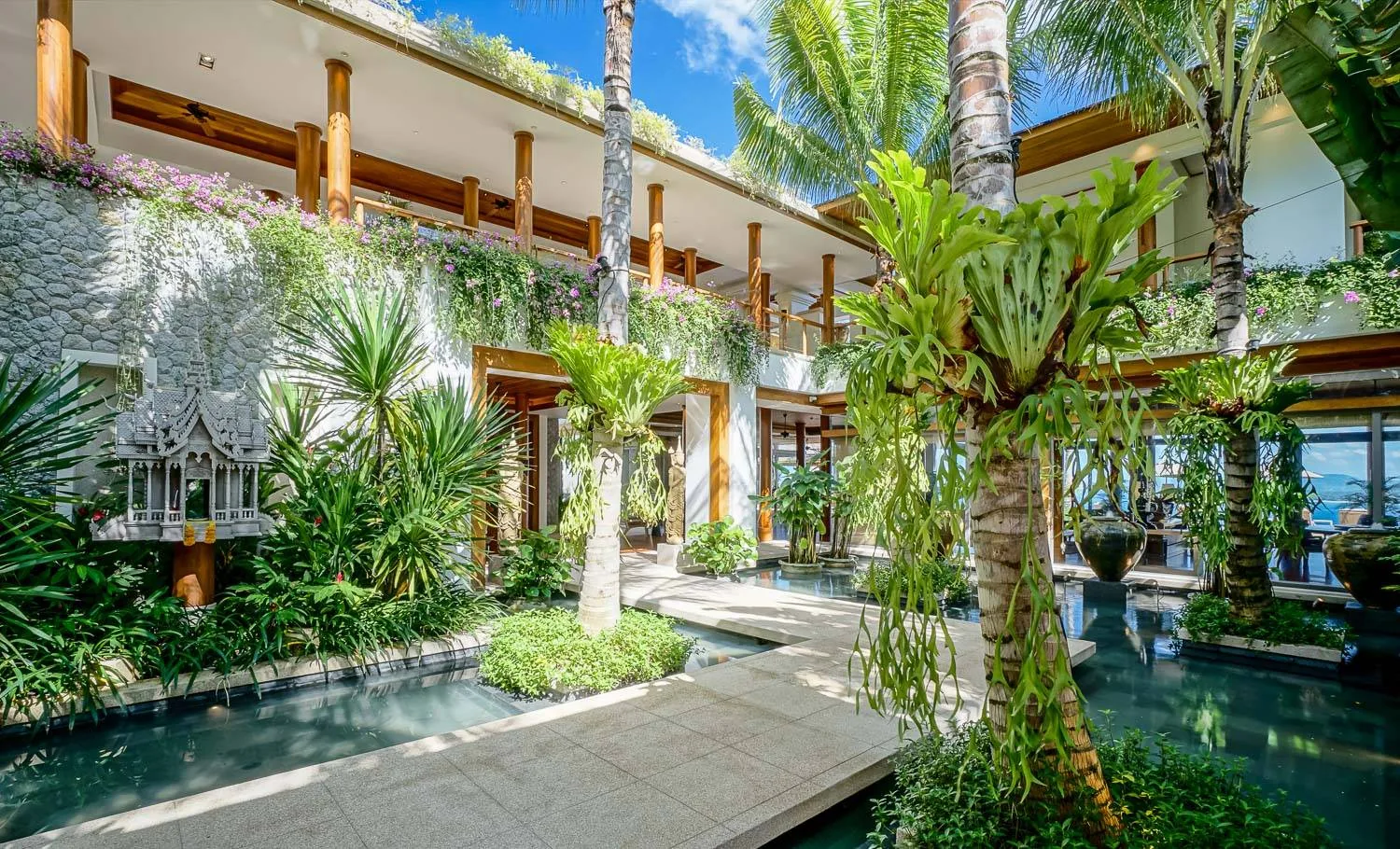 An outdoor walkway beside a pond with a palm tree, on stone paving
