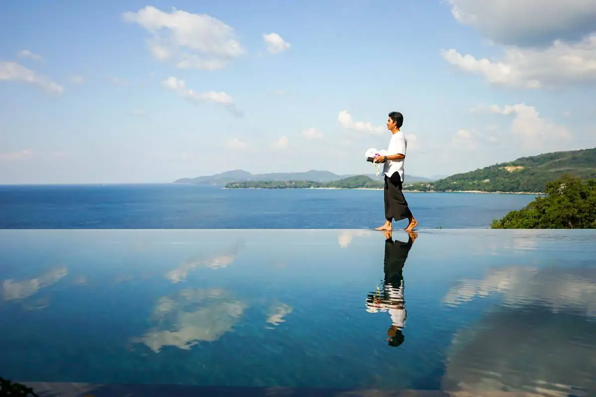 Villa staff carrying towels along the infinity pool edge above the sea