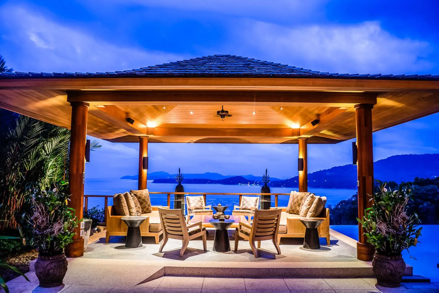 A timber pavilion lounge area at dusk with the sea visible beyond