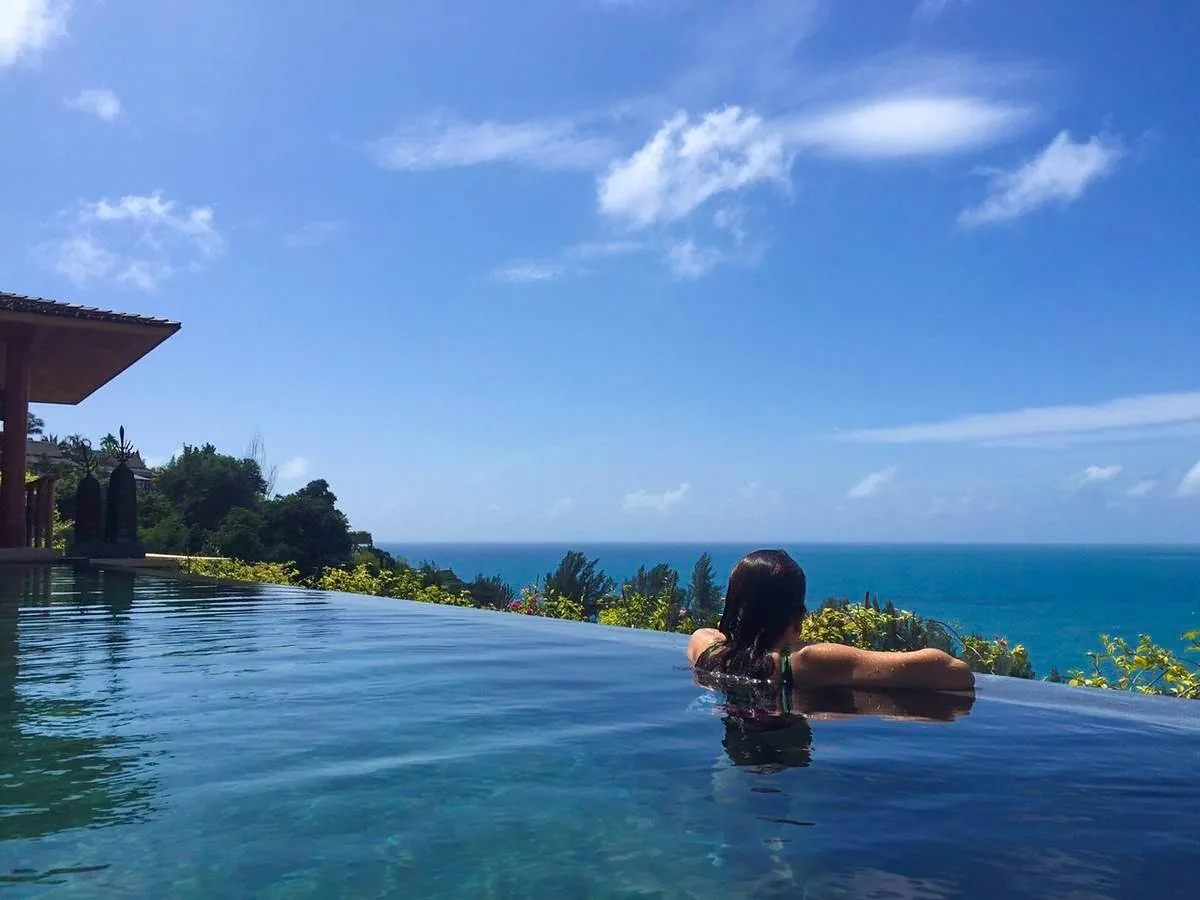 An infinity pool with a person swimming, overlooking the sea